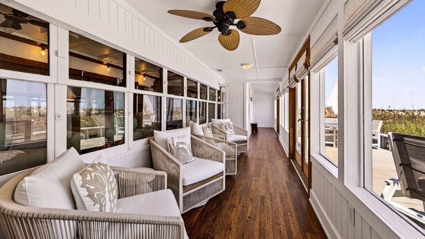 A covered outdoor seating area with wicker furniture, large windows, and a ceiling fan. - One-of-a-Kind Trolley Home, Oceanfront w/ Dune View by Tybee Cottages (Tybee Island)