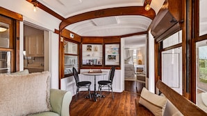 A cozy interior with a wooden ceiling, a dining area with a table and chairs, and a view of the kitchen through an open door. - One-of-a-Kind Trolley Home, Oceanfront w/ Dune View by Tybee Cottages (Tybee Island)