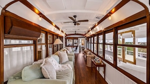 A narrow, elongated room with a wooden ceiling, a ceiling fan, and a sofa with cushions. - One-of-a-Kind Trolley Home, Oceanfront w/ Dune View by Tybee Cottages (Tybee Island)