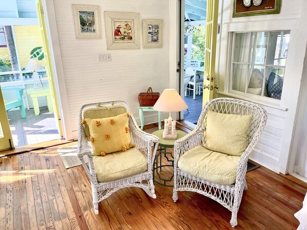 A room with two wicker chairs, a small table with a lamp, and a door leading outside.
