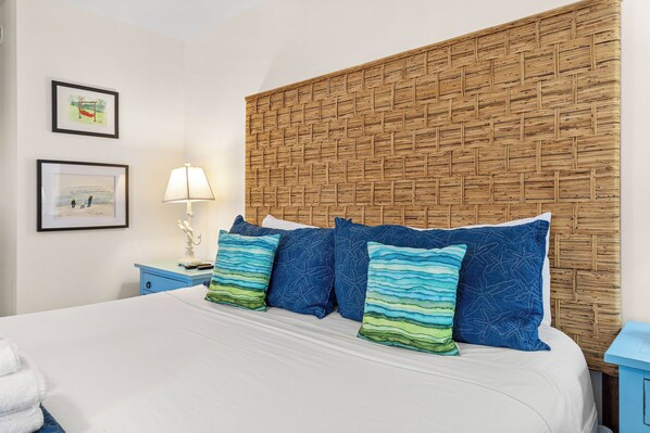 A bed with a white sheet, a blue nightstand with a lamp, and a wall with two framed pictures. - Private Pool + 2 Blocks to Beach + Pet Friendly by Tybee Cottages (Tybee Island)