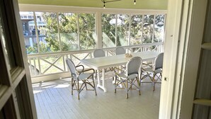 A covered outdoor patio with a white table and chairs, surrounded by a white railing. - Large, Classic Beachfront House with Wrap-Around Porch by Tybee Cottages (Tybee Island)