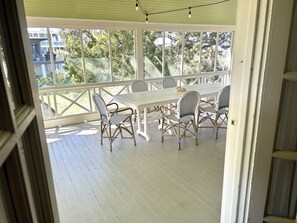 A covered outdoor patio with a white table and chairs, surrounded by a white railing.