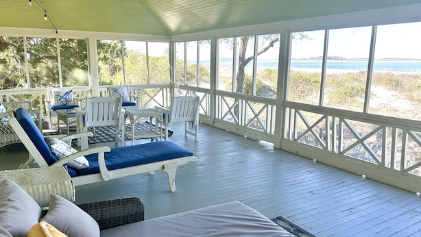 A covered outdoor seating area with white furniture and a view of the beach. - Large, Classic Beachfront House with Wrap-Around Porch by Tybee Cottages (Tybee Island)