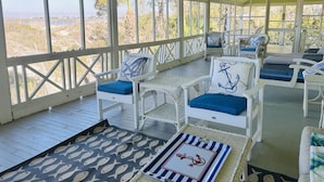 A covered outdoor seating area with white wicker furniture and blue cushions, overlooking a natural landscape. - Large, Classic Beachfront House with Wrap-Around Porch by Tybee Cottages (Tybee Island)