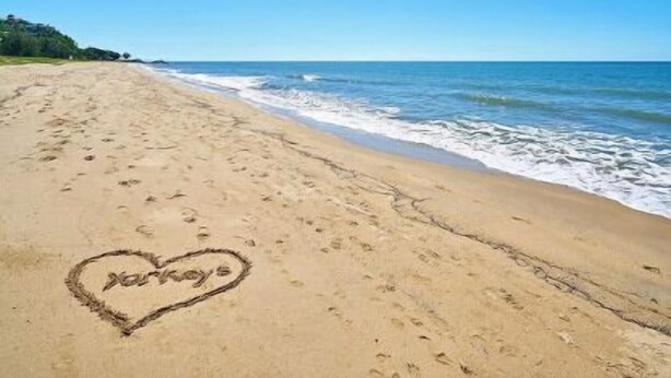 Una playa con huellas y un corazón dibujado en la arena.