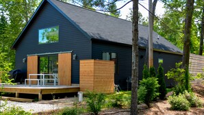 A modern house with a dark exterior, a wooden deck, and a large window. - Modern home in Glen Arbor. Steam shower. Walk to lake. Air conditioning. (Glen Arbor)