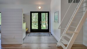 A modern interior with a wooden floor, a black door with glass panels, a white wall with a picture, and a white staircase. - Modern home in Glen Arbor. Steam shower. Walk to lake. Air conditioning. (Glen Arbor)