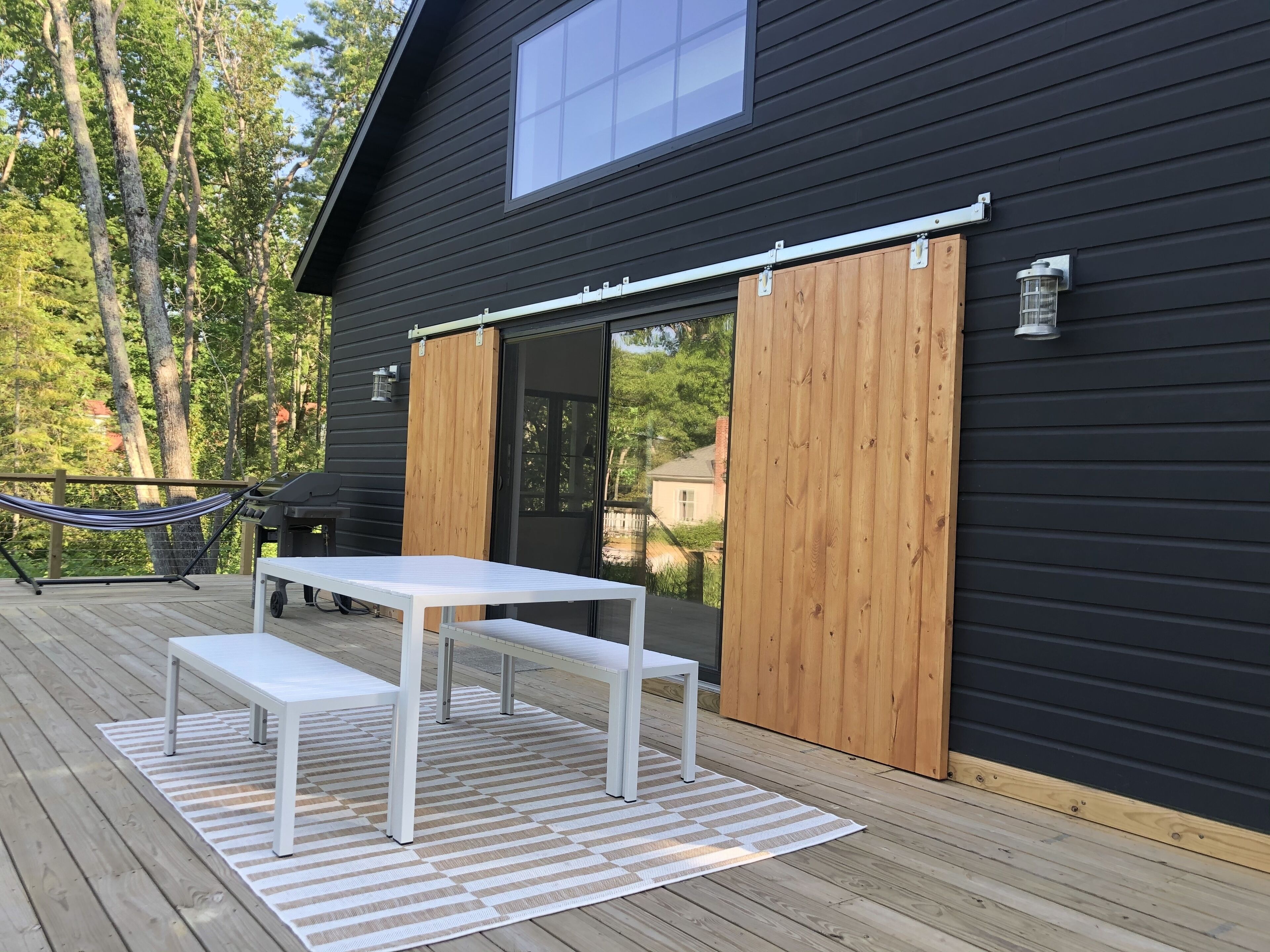 Een terras met een witte tafel en banken, een hangmat en een barbecue.