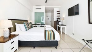 Una habitació d'hotel amb llit, taula de nit, làmpada, televisió i ventilador de sostre.