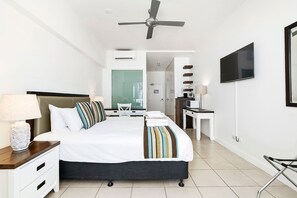 Quarto de hotel com cama, mesa de cabeceira, luminária, televisão e ventoinha no teto.