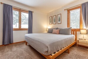Une chambre à coucher avec un lit, deux fenêtres, une table de chevet et une lampe.