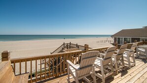 Una terraza de madera con sillas Adirondack blancas con vistas a la playa.
