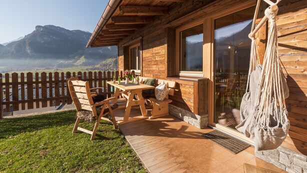 A wooden cabin with a patio, a hammock, and a view of mountains.
