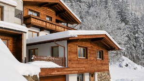 A wooden chalet with a balcony, a stone wall, and a snow-covered landscape.