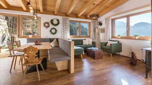 A cozy cabin interior with wooden beams, a dining area, a sofa, and a view of mountains.