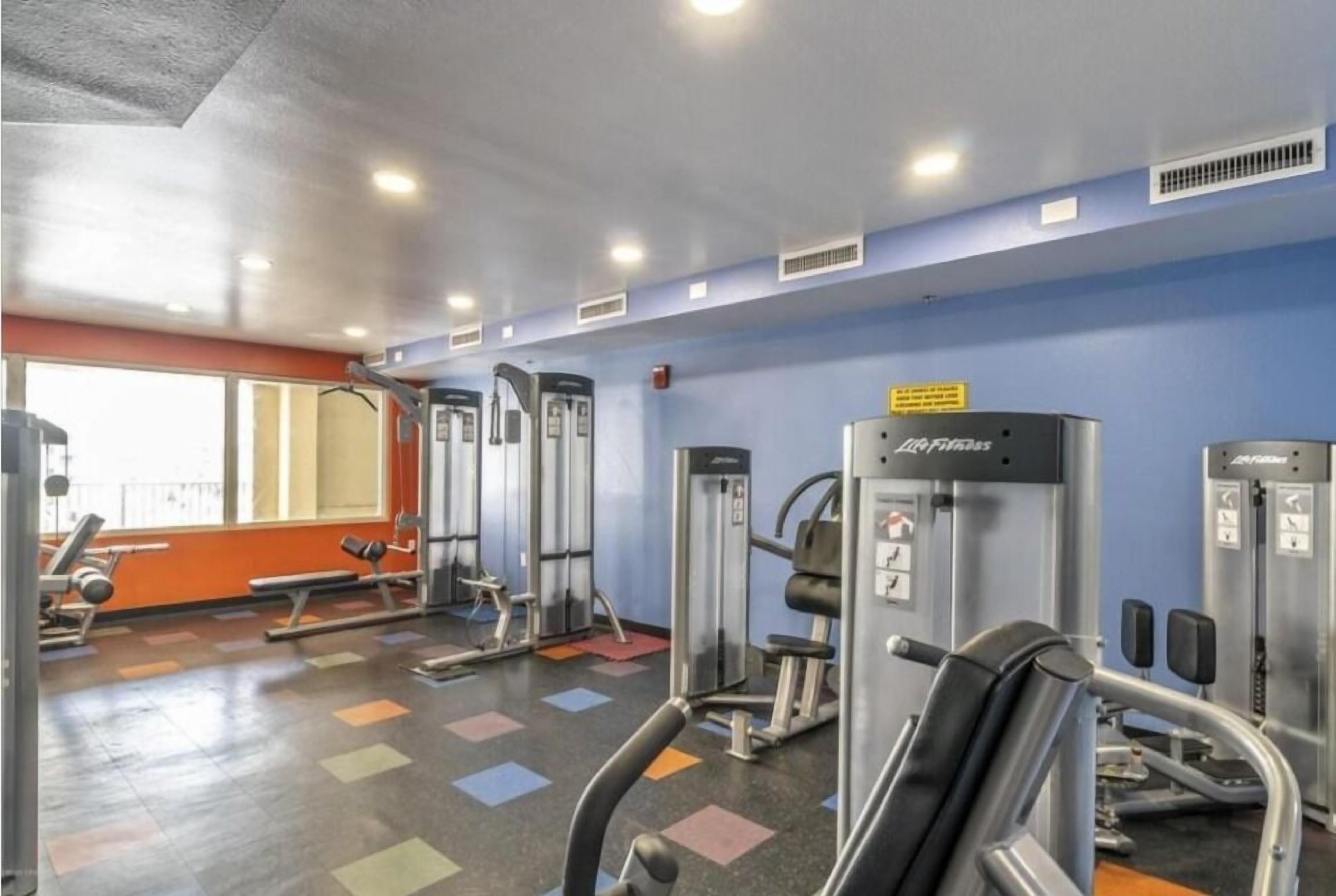 A gym with various exercise machines, a bench, and a colorful floor.
