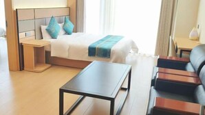 Een hotelkamer met een bed, nachtkastje, een klein tafeltje, een bank en een raam met gordijnen.