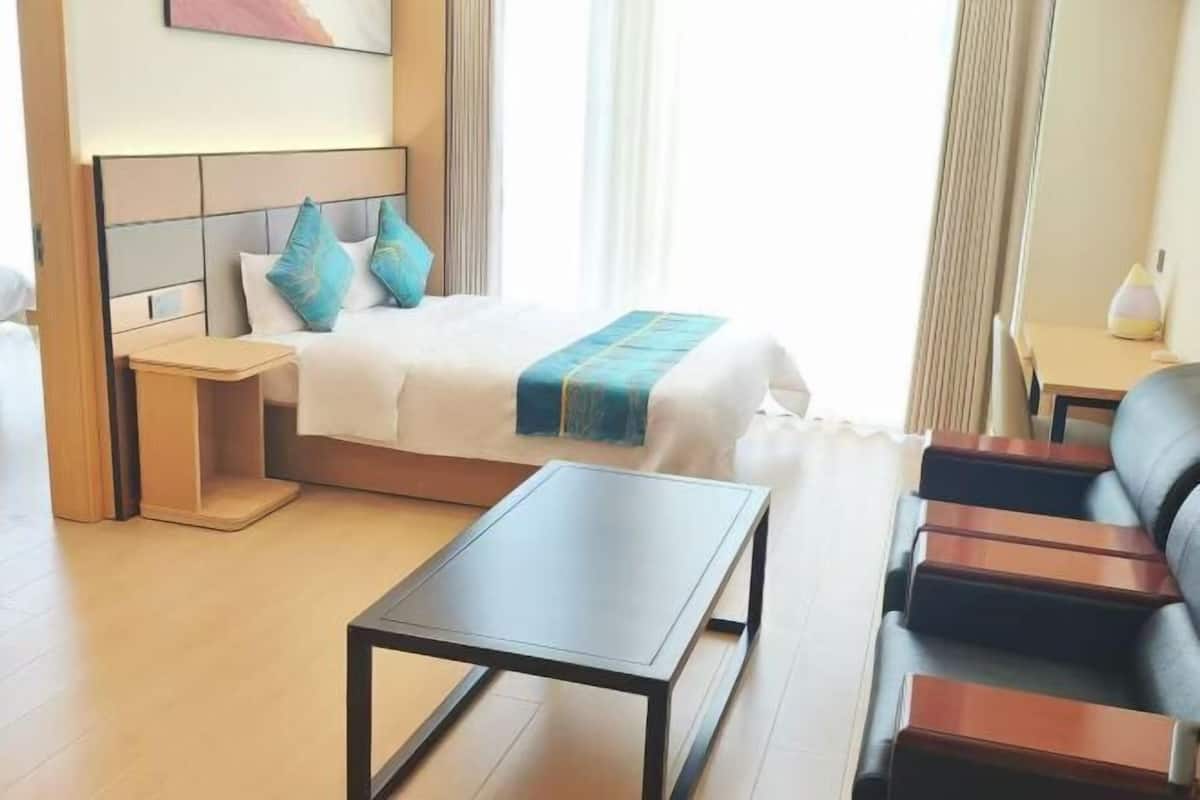 A hotel room with a bed, bedside table, a small table, a sofa, and a window with curtains.
