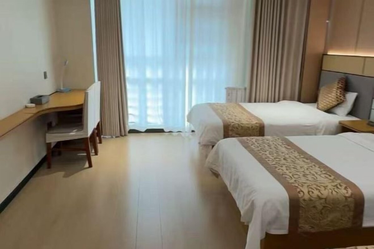 Une chambre d’hôtel avec deux lits, un bureau et une fenêtre avec des rideaux.