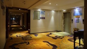 A hotel corridor with patterned carpet, a reception area, and a door with a sign. - Damojin Hotel (Jinchang)