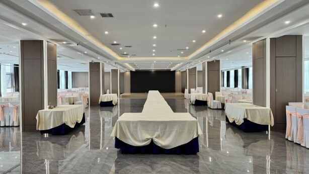 A spacious banquet hall with a long table at the center, surrounded by smaller tables with white tablecloths and pink sashes. - Damojin Hotel (Jinchang)