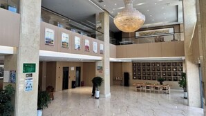 Een ruime lobby met een kroonluchter, een zithoek en een wand vol ingelijste foto's.