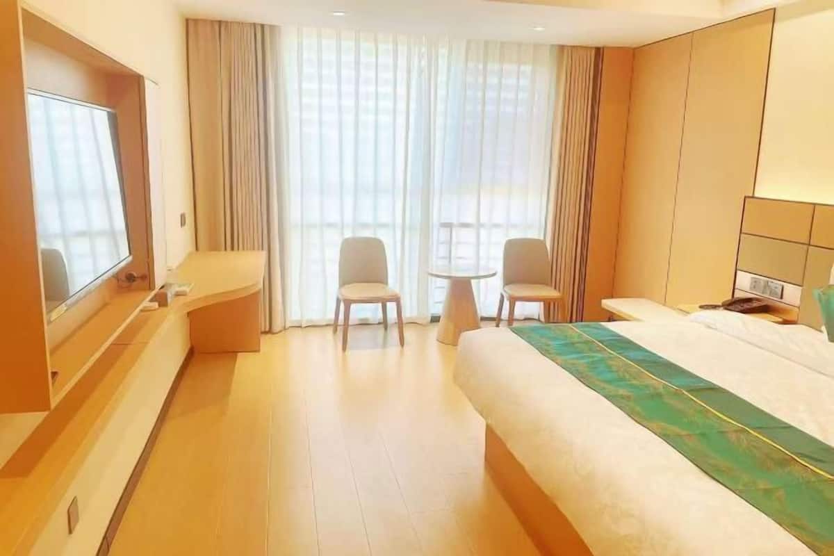 A hotel room with a bed, two chairs, a small table, a TV, and a large window with curtains.