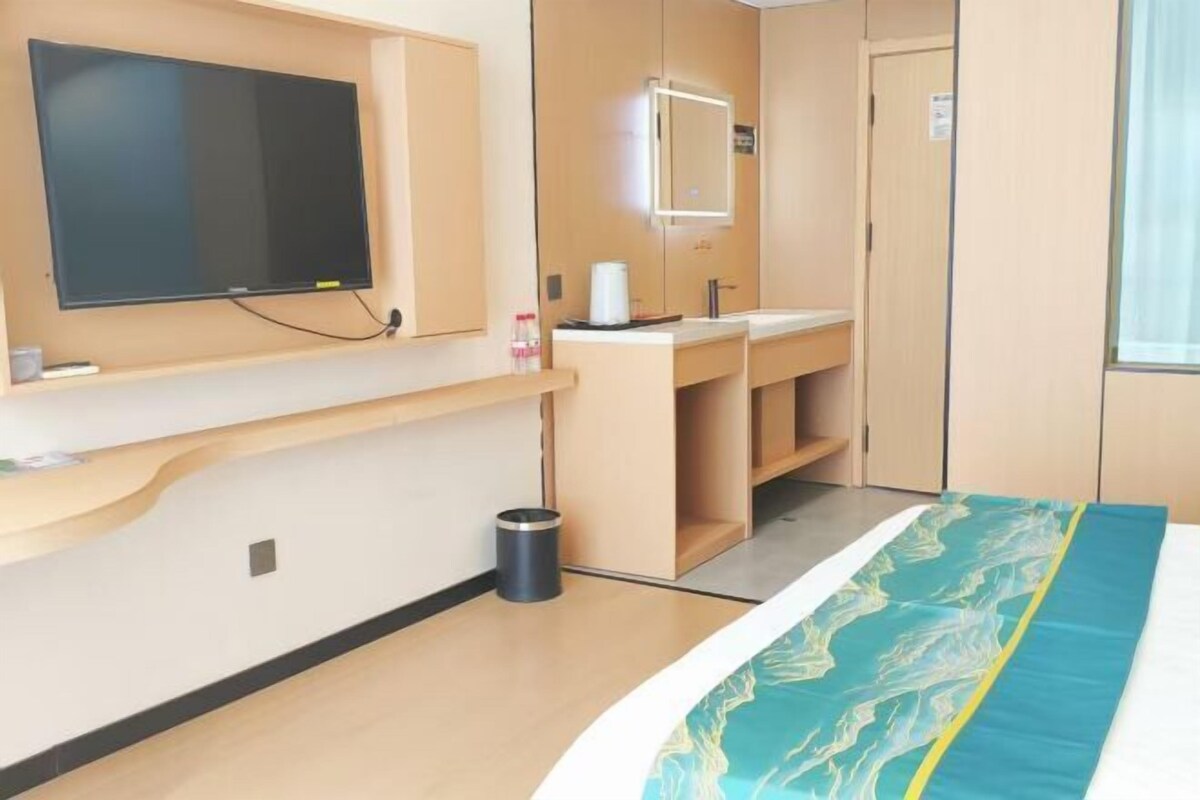 Une chambre d’hôtel avec un lit, un téléviseur fixé au mur, une salle de bain avec un miroir et une poubelle.