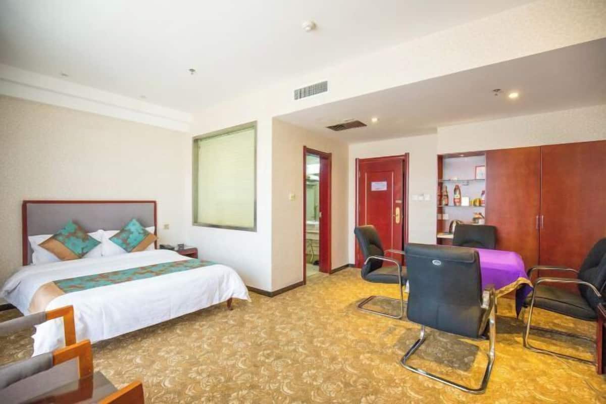 A hotel room with a bed, two chairs, a desk, and a wardrobe.