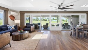 Amplia sala de estar con ventilador de techo, una mesa de comedor con sillas y vista a un jardín exuberante a través de puertas correderas de vidrio.