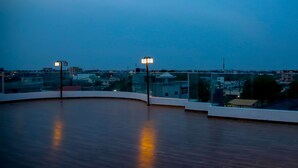 Una terrazza sul tetto con pavimento in legno curvo, ringhiere in vetro e due lampioni.
