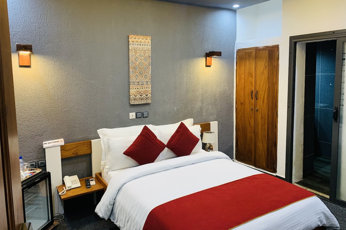 A hotel room with a bed, a bedside table with a phone, a lamp, and a wall-mounted decorative piece.