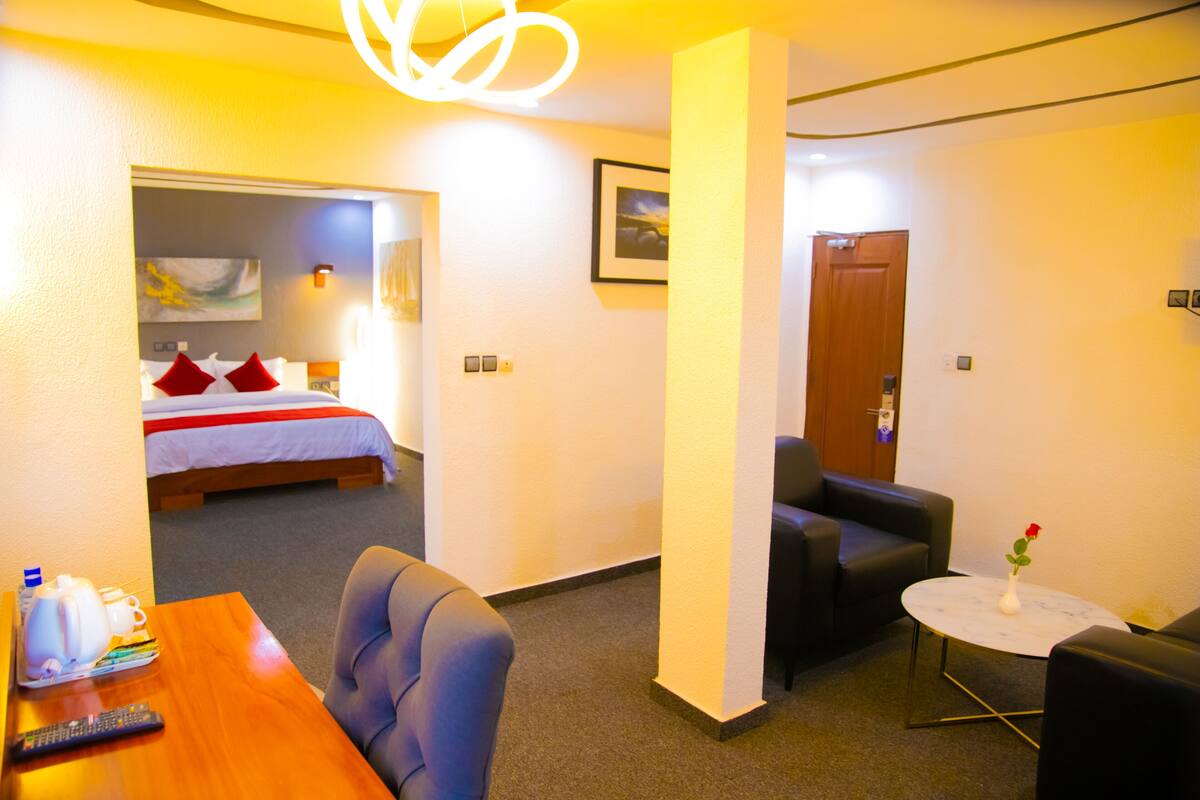 A hotel room with a bed, a desk with a remote control, a coffee maker, and a vase with a flower.