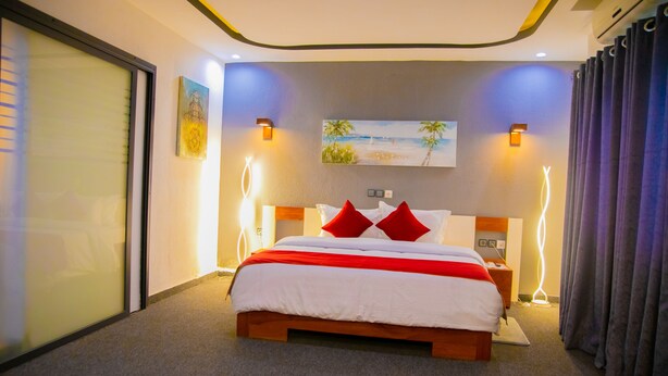 Una camera d'albergo moderna con un letto grande, due cuscini rossi, un quadro che raffigura una spiaggia e una porta scorrevole.