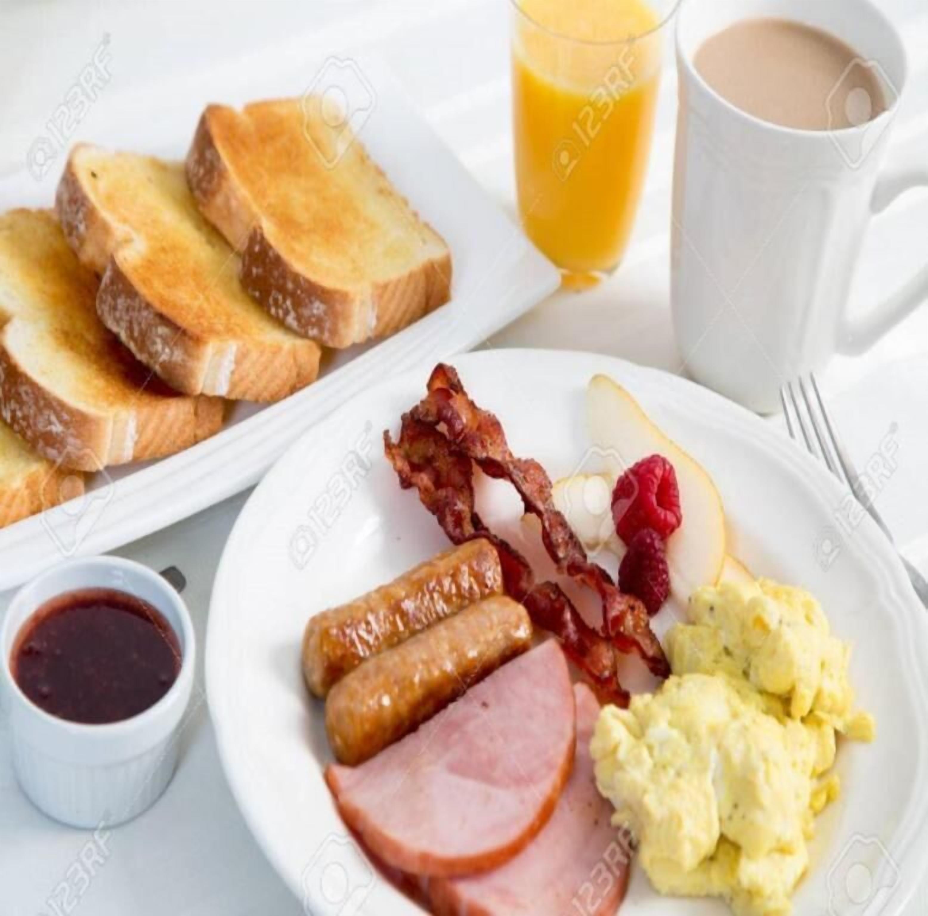 A breakfast plate with toast, sausages, bacon, ham, scrambled eggs, raspberries, and a glass of orange juice.