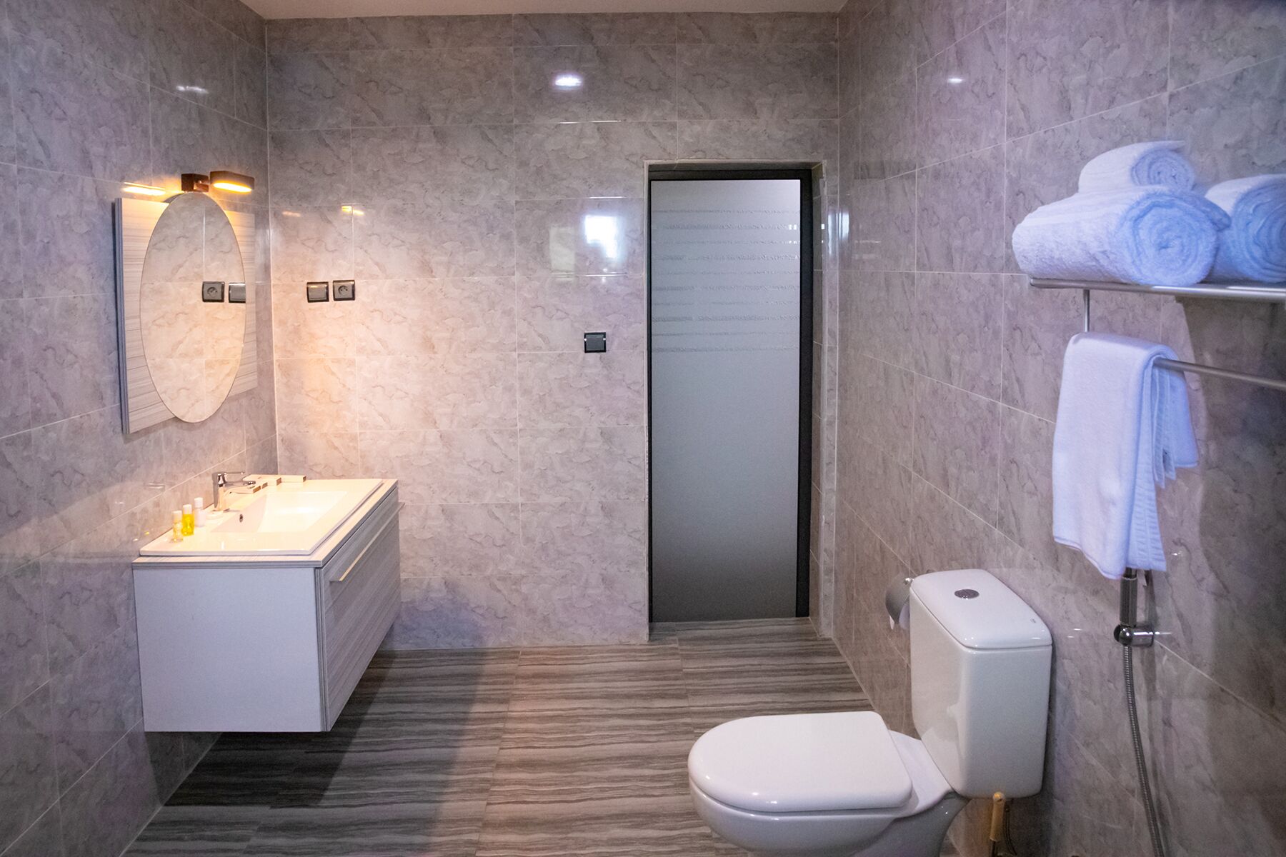 Un baño moderno con piso de mármol, un lavamanos blanco, inodoro y toallero con toallas.