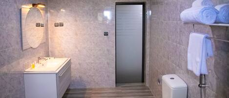 Un baño moderno con piso de mármol, un lavamanos blanco, inodoro y toallero con toallas.