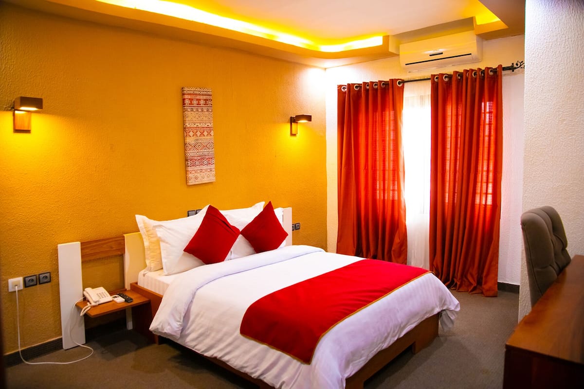 A hotel room with a bed, a desk, a telephone, and a wall-mounted air conditioner.