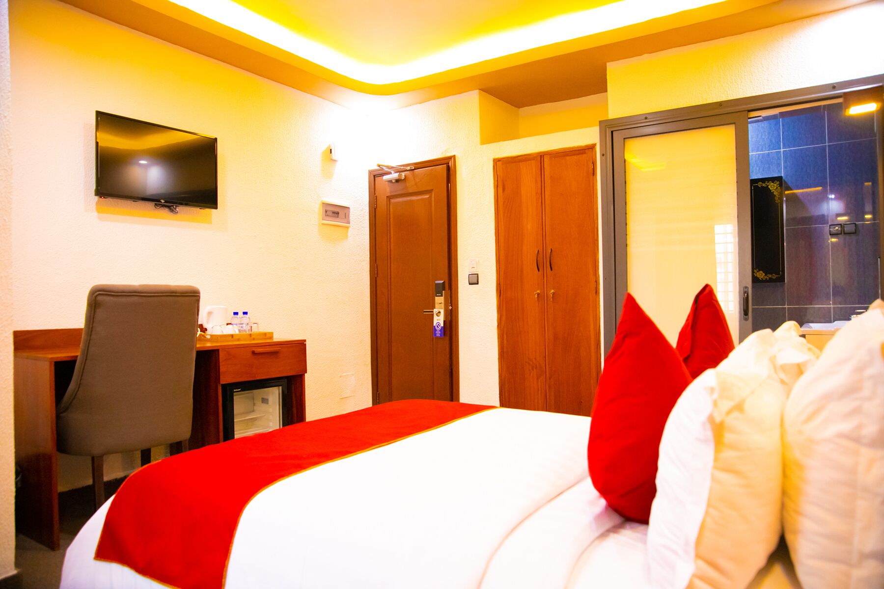 A hotel room with a bed, a desk, a chair, and a television on the wall.