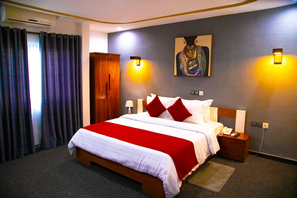 A hotel room with a large bed, a wooden wardrobe, a painting on the wall, and two bedside lamps.