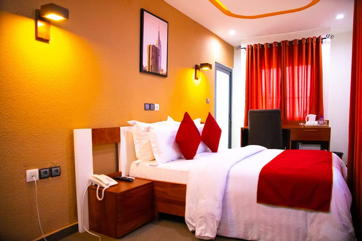 A hotel room with a bed, a desk, a chair, a phone, and a picture on the wall.