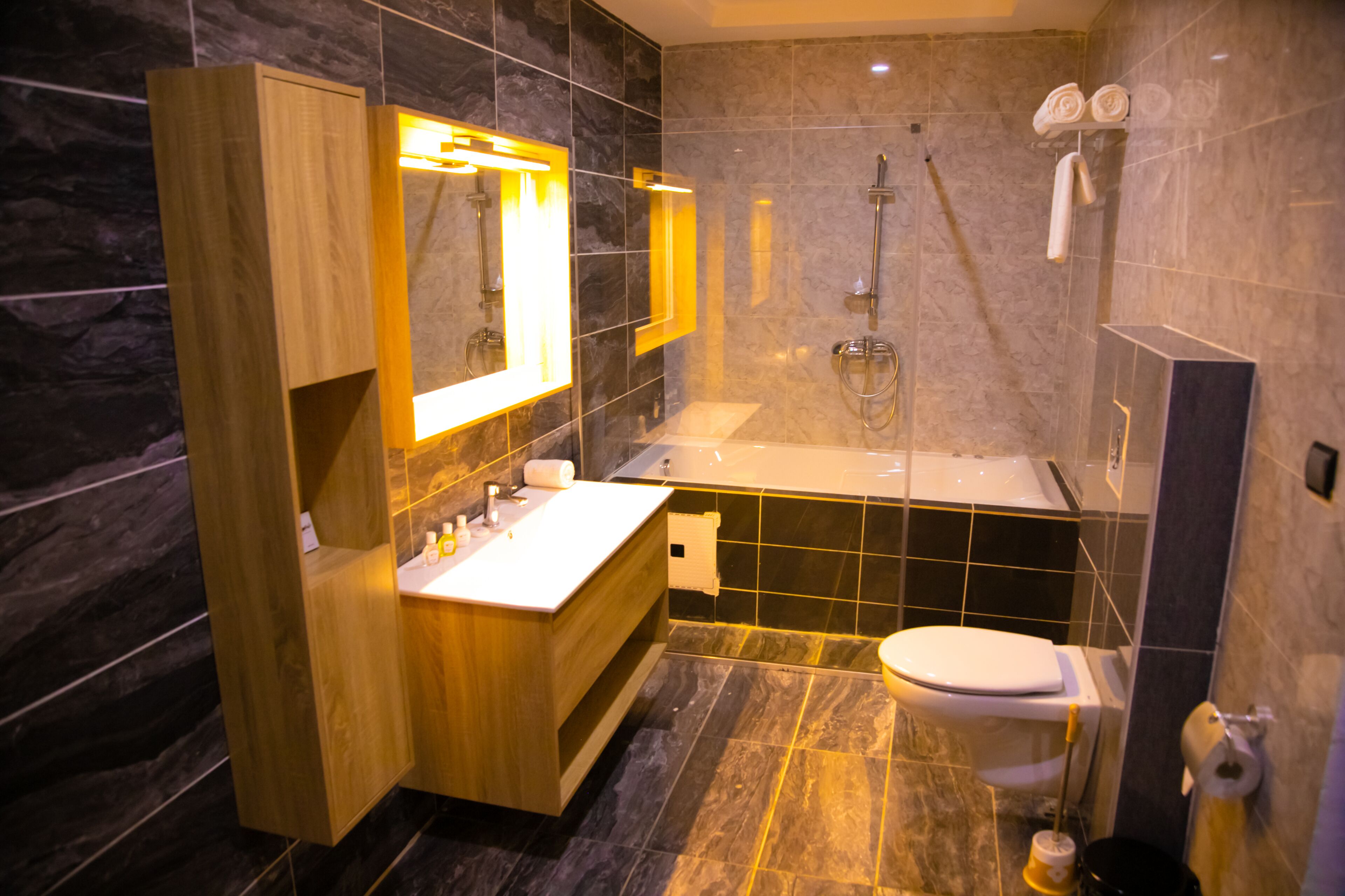 Un baño moderno con tocador de madera, un espejo grande, una bañera y un inodoro.