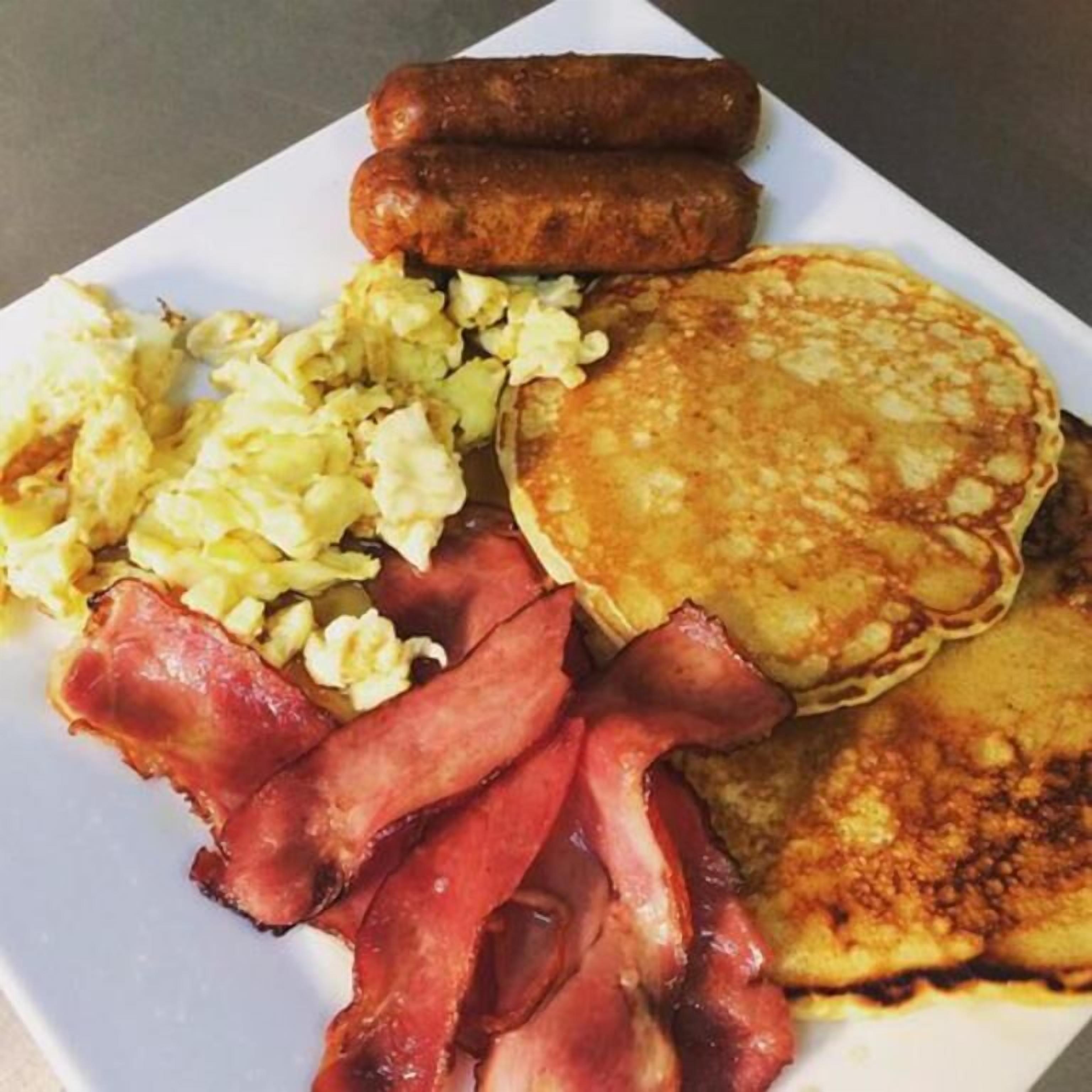 A plate with pancakes, sausages, scrambled eggs, and bacon.