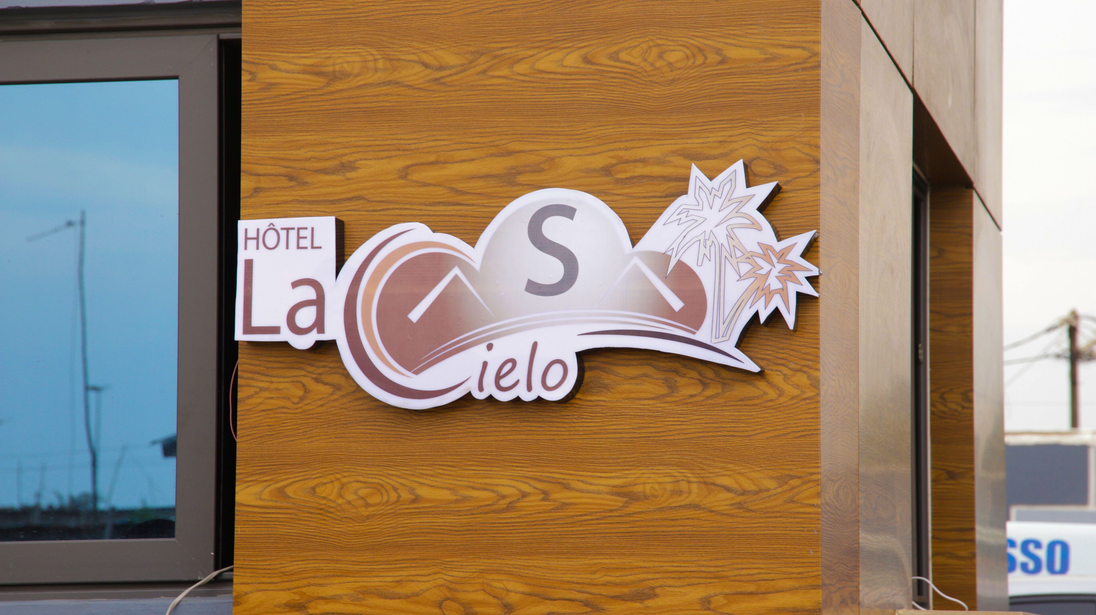 A wooden sign with the text "HOTEL La Cielo" and decorative elements including a mountain and palm tree.