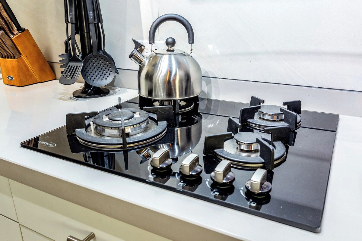 A modern kitchen with a stainless steel kettle, a gas stove with four burners, and a set of kitchen utensils.
