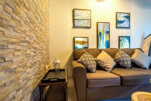 Ein Wohnzimmer mit einer Steinwand, einem braunen Sofa mit gemusterten Kissen und gerahmten Kunstwerken an der Wand.