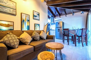 A modern living room with a sofa, a round wooden coffee table, and a dining area with striped chairs.