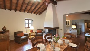 A dining area with a wooden table set for four, surrounded by chairs, a fireplace, and a view of the kitchen. - Dionisia, Capannole, Gaiole in Chianti, Siena and Chianti (Gaiole in Chianti)