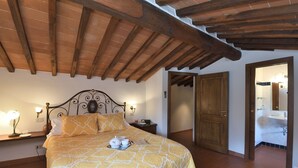 A bedroom with a wooden ceiling, a bed with a patterned bedspread, bedside lamps, and a nightstand. - Dionisia, Capannole, Gaiole in Chianti, Siena and Chianti (Gaiole in Chianti)